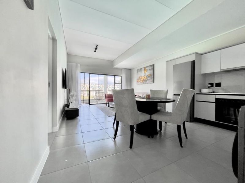 Modern open-plan living and dining area featuring sleek tiled floors, a contemporary kitchen with built-in appliances, and large sliding doors leading to a balcony.