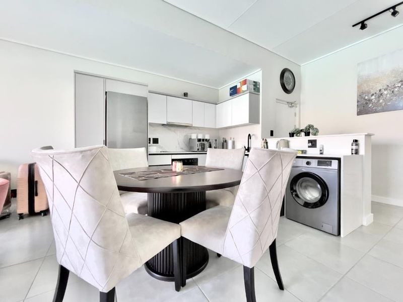 Modern open-plan kitchen and dining area featuring sleek cabinetry, integrated appliances, a built-in washing machine, and contemporary tiled flooring.