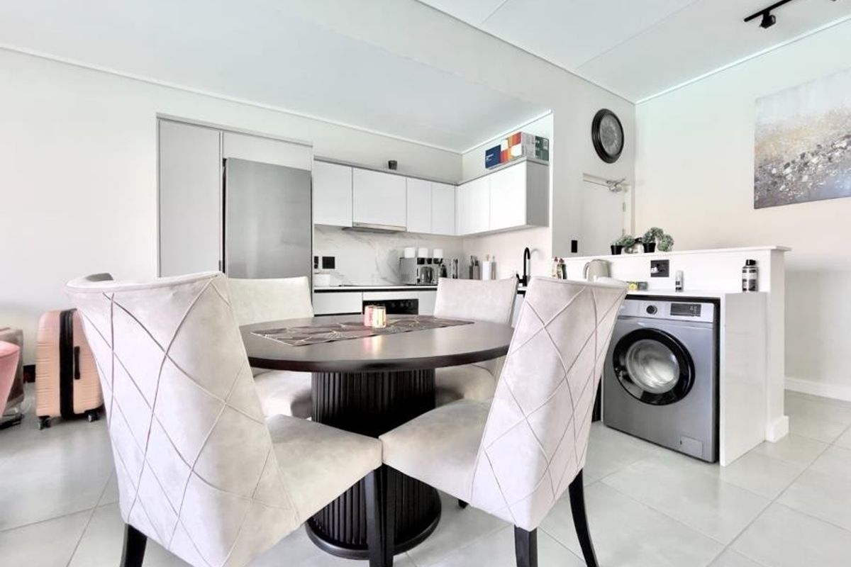 Modern open-plan kitchen and dining area featuring sleek cabinetry, integrated appliances, a built-in washing machine, and contemporary tiled flooring.
