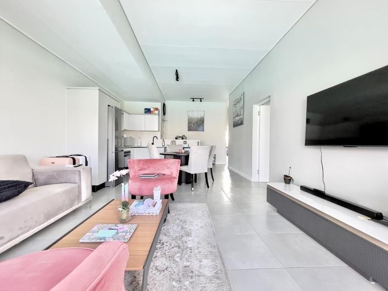 A bright open-plan living and kitchen area featuring modern tiled flooring, neutral walls, and a functional kitchen layout with built-in cabinetry.