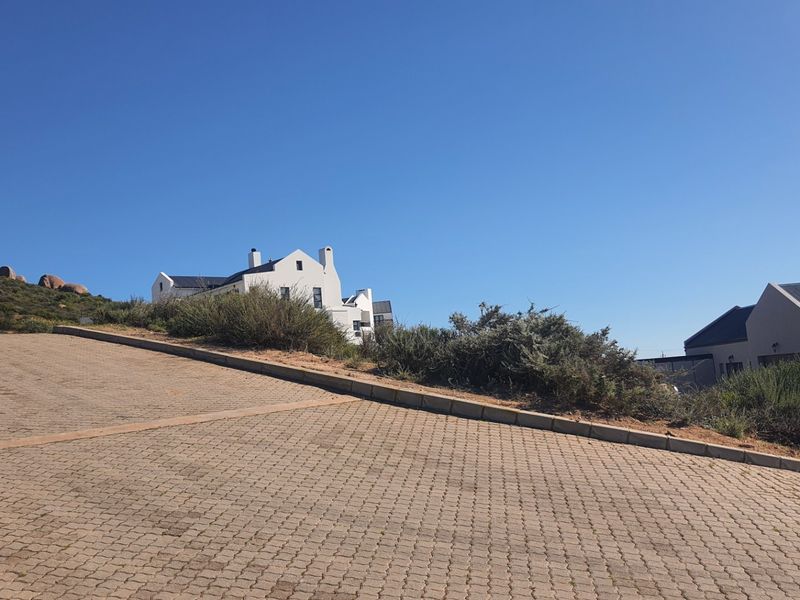 A view of a paved residential driveway and surrounding landscape, showing the approach to nearby properties.