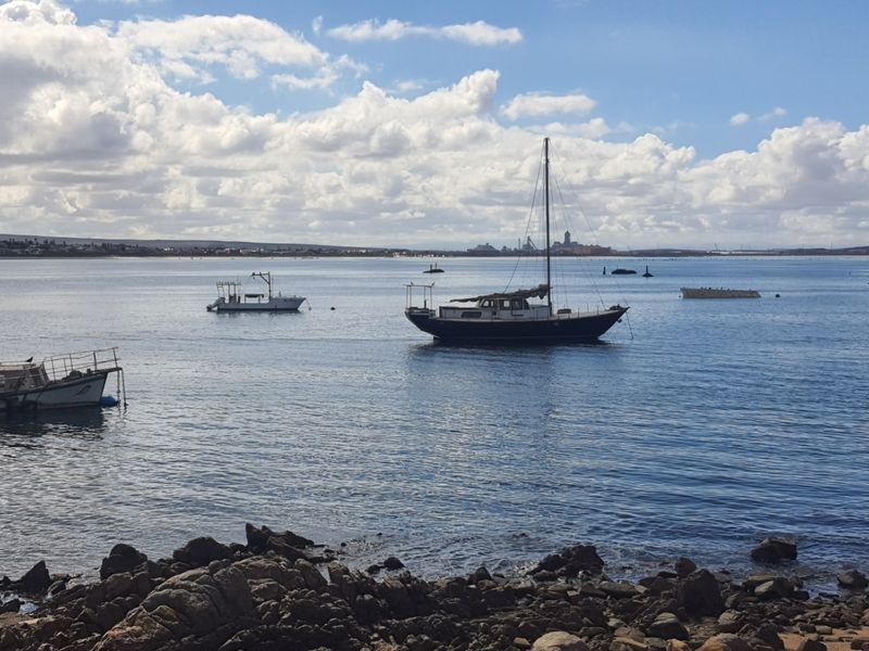 A scenic coastal view overlooking the bay with anchored boats and a rocky shoreline in the foreground.