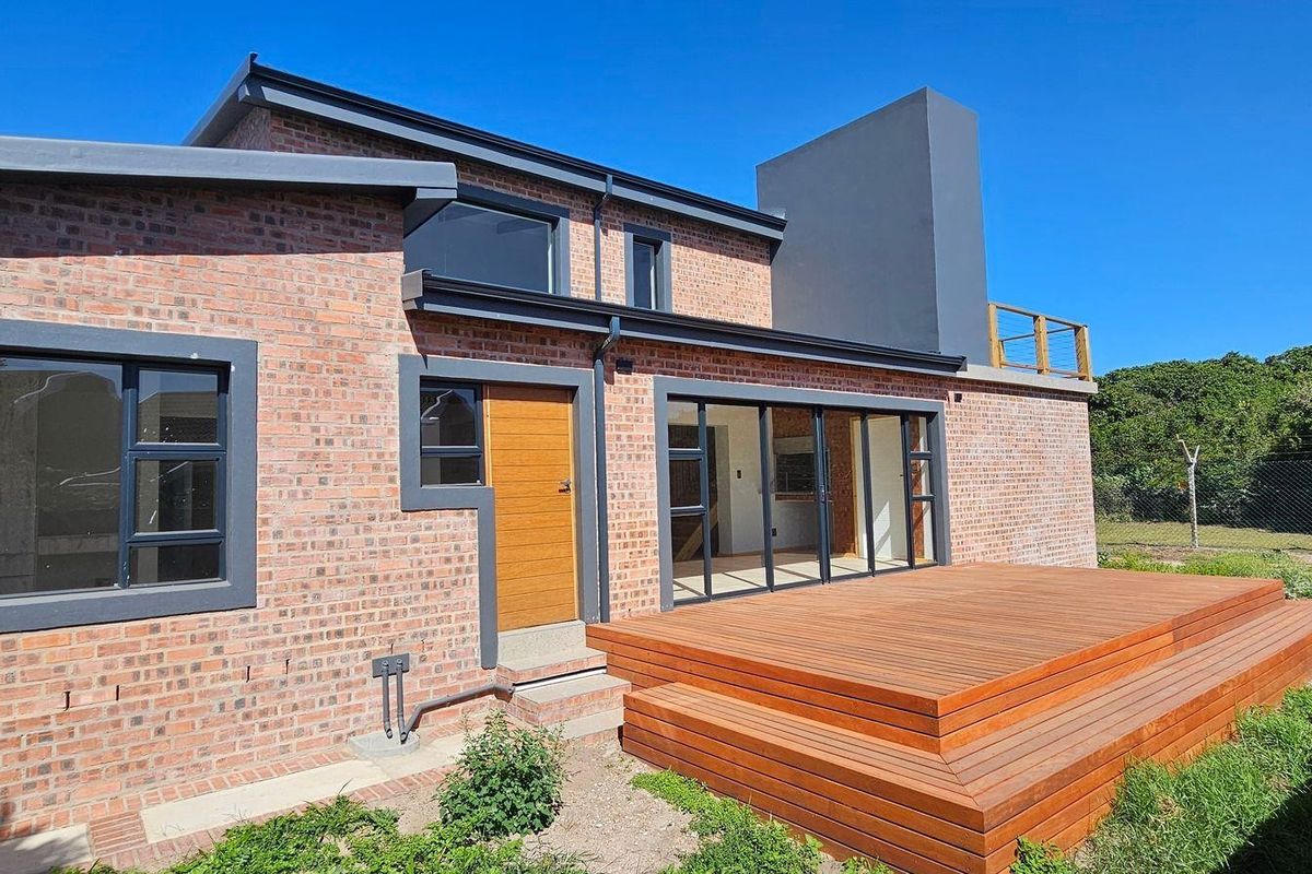 Modern rear elevation featuring exposed brickwork, expansive timber decking, and large sliding glass doors leading to the interior living space.