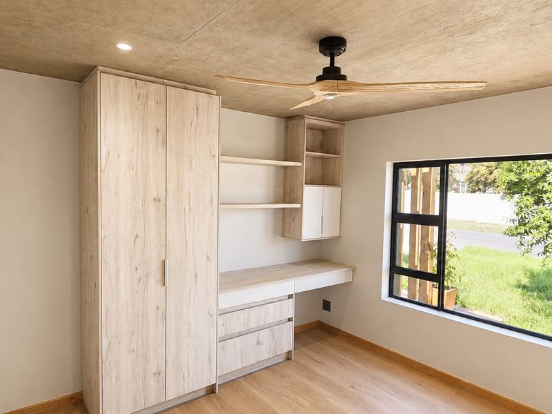 Modern bedroom featuring built-in cabinetry, a desk area, ceiling fan, and large window with garden views.
