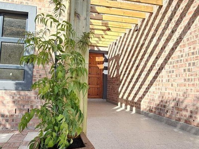 A well-maintained outdoor patio area featuring a timber pergola, brick exterior walls, and paved flooring, providing a clean and structured transition space.