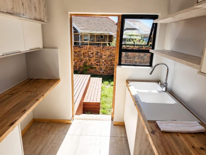 A modern, well-lit scullery featuring sleek built-in cabinetry, wooden countertops, and an undermount sink with direct access to the rear garden.
