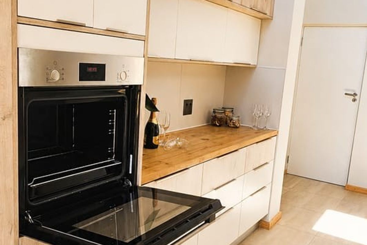 Modern kitchen featuring light wood-tone cabinetry, integrated oven, wooden countertops, and large format floor tiles with natural light from a skylight.
