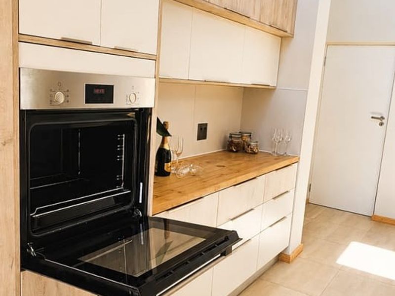 Modern kitchen featuring light wood-tone cabinetry, integrated oven, wooden countertops, and large format floor tiles with natural light from a skylight.