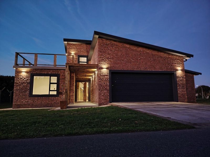 Modern double-story brick home featuring a double garage, upper-level balcony, and timber pergola entrance, captured at dusk with exterior accent lighting.
