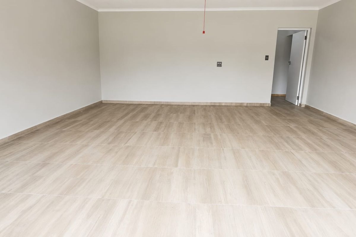 A spacious, empty living area featuring modern wood-look tile flooring, neutral wall finishes, and a clean, minimalist aesthetic ready for furnishing.