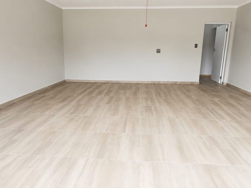A spacious, empty living area featuring modern wood-look tile flooring, neutral wall finishes, and a clean, minimalist aesthetic ready for furnishing.