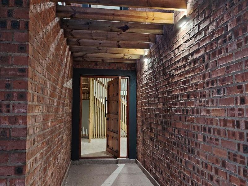 A striking entrance featuring exposed brick walls, a timber pergola overhead, and stone flooring leading to a solid timber front door.