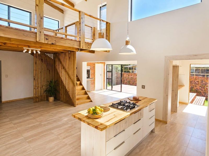 Spacious open-plan living area featuring a modern kitchen island with gas hob, timber staircase, and mezzanine level with high ceilings and natural light.