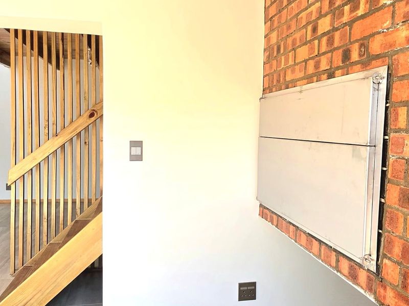 A bright living area featuring an exposed brick wall with a built-in fireplace and a wooden staircase with a timber balustrade.