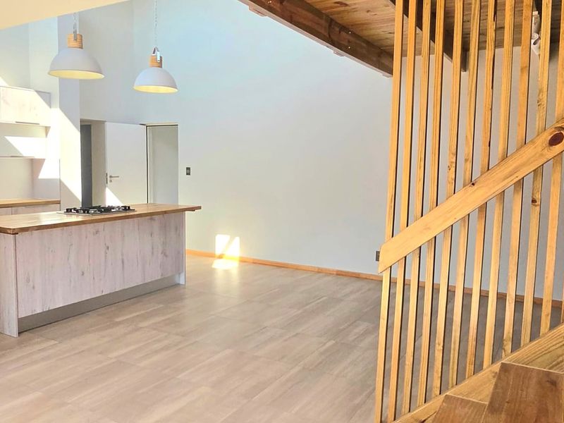 Spacious open-plan living area featuring a modern kitchen island with integrated hob, vaulted ceilings, and a striking timber staircase with wooden balustrade.