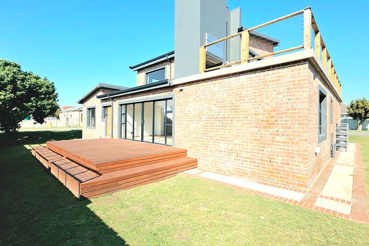 Rear view of a modern brick house featuring a timber deck, large sliding glass doors, and an upper-level rooftop terrace with a timber balustrade.