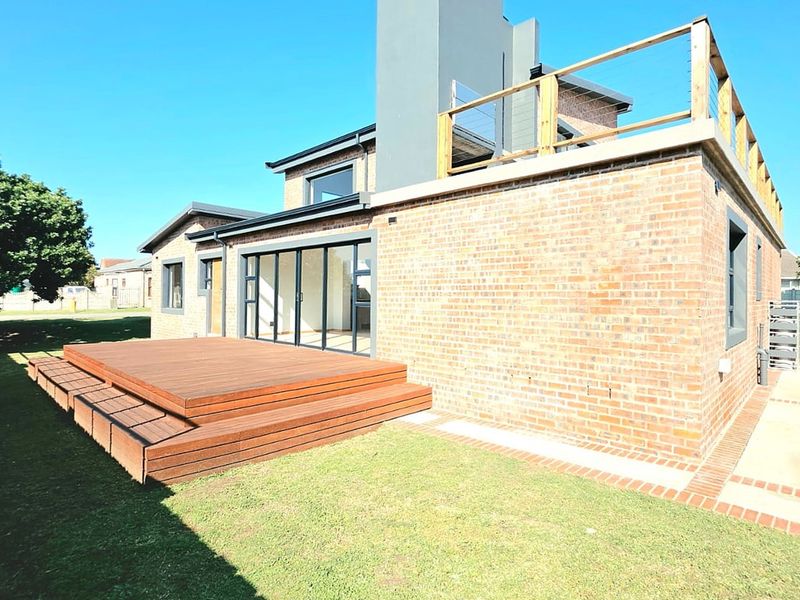 Rear view of a modern brick house featuring a timber deck, large sliding glass doors, and an upper-level rooftop terrace with a timber balustrade.