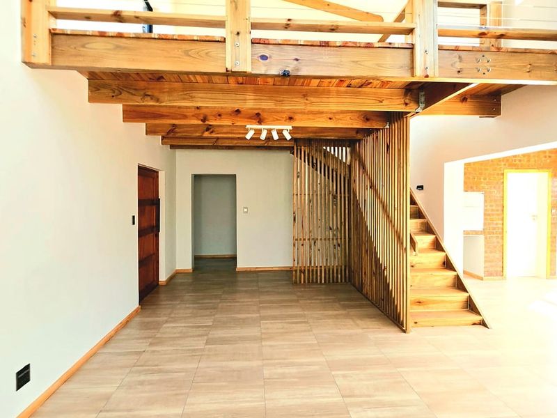 Spacious open-plan living area featuring a timber staircase, mezzanine level, exposed brick accents, and modern tiled flooring.