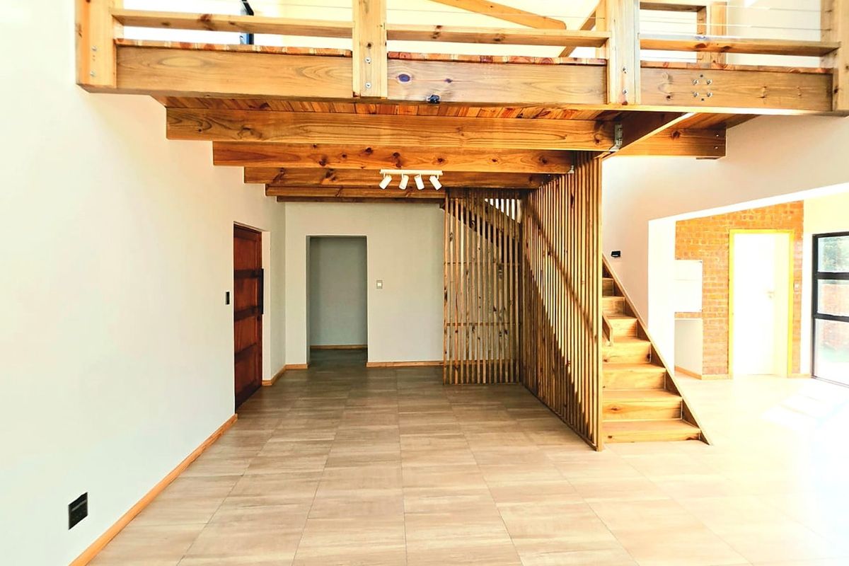Spacious open-plan living area featuring a timber staircase, mezzanine level, exposed brick accents, and modern tiled flooring.