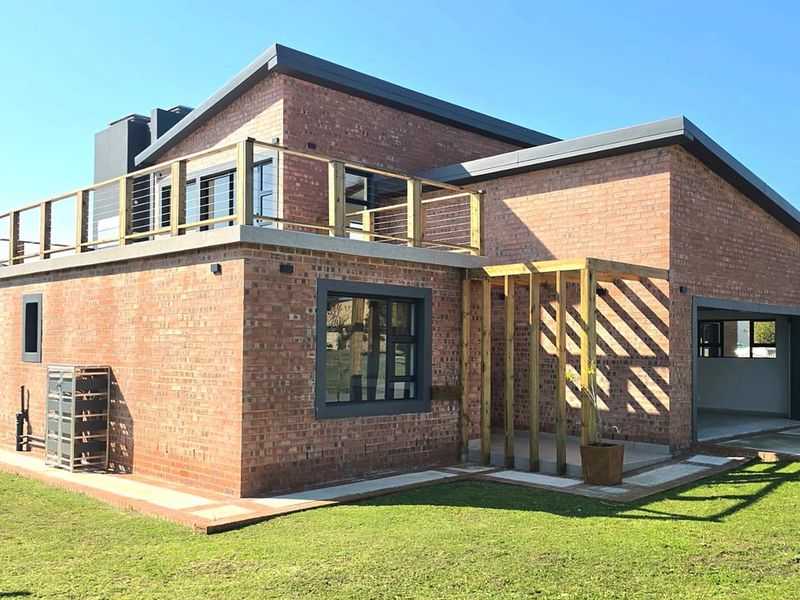 Modern double-storey house featuring exposed brickwork, a spacious upper-level balcony, timber pergola, and an integrated garage set within a landscaped garden.