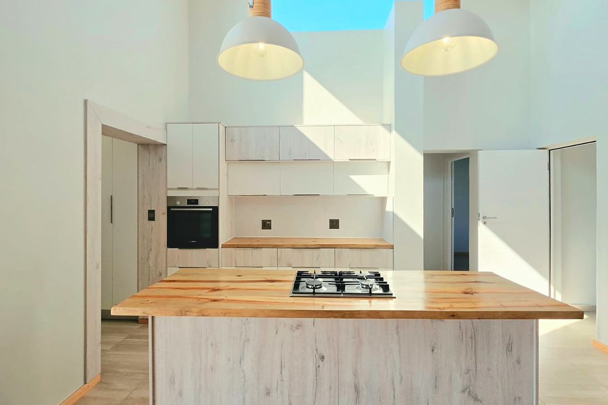 Modern kitchen featuring a central island with a gas hob, light wood cabinetry, wooden countertops, and a bright skylight overhead.