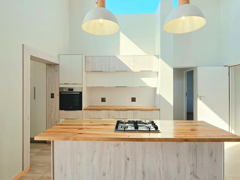 Modern kitchen featuring a central island with a gas hob, light wood cabinetry, wooden countertops, and a bright skylight overhead.