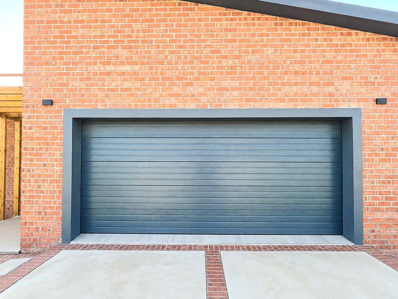 Modern brick exterior featuring a large sectional garage door, concrete driveway, and an adjacent timber pergola structure.
