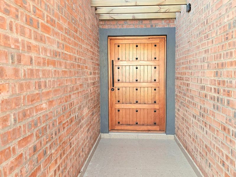 A secure and well-maintained entrance featuring exposed brick walls, a solid timber front door, and a decorative timber pergola overhead.