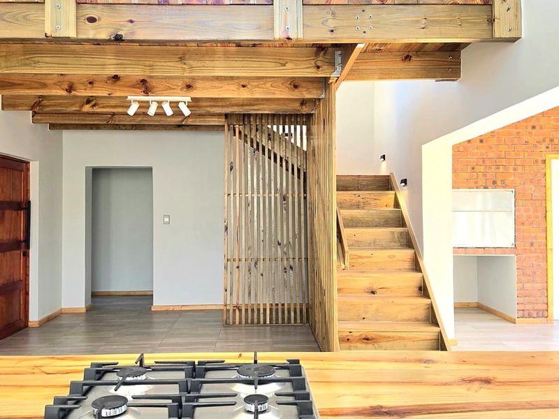 Open plan living area featuring exposed timber beams, a wooden staircase with slat screen, and a modern gas hob set into a timber countertop.