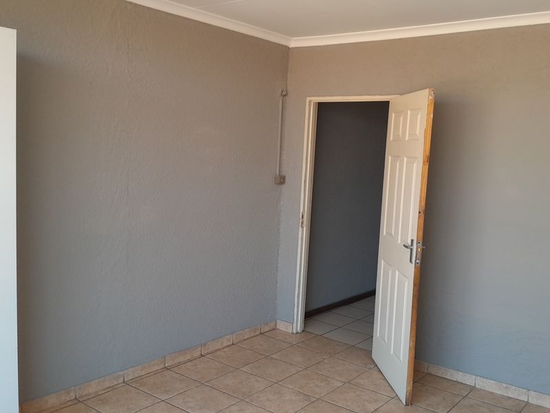 An empty bedroom featuring tiled flooring and a neutral grey wall finish, ready for personalization.