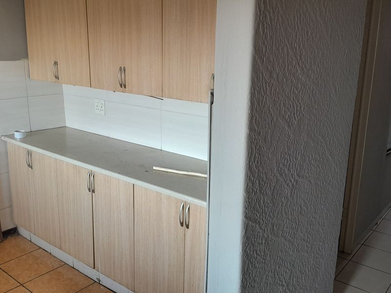 A compact kitchen area featuring light wood-look cabinetry, a tiled backsplash, and ceramic flooring, presenting a functional space ready for modern updates.