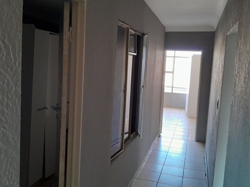 A vacant hallway featuring tiled flooring, built-in storage cupboards, and an internal window, leading towards a bright living area.