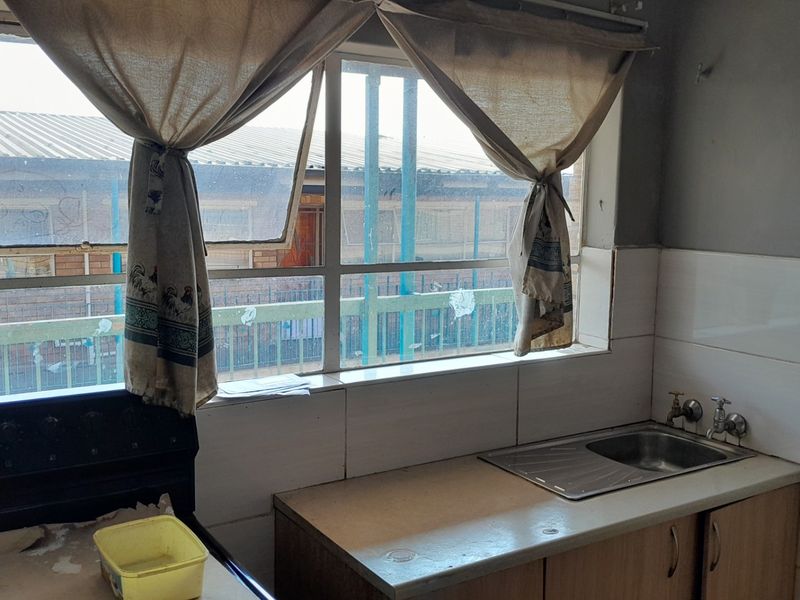 A dated kitchen area featuring a stainless steel sink, tiled splashback, and built-in cabinetry, requiring cosmetic updates to improve functionality and aesthetic appeal.