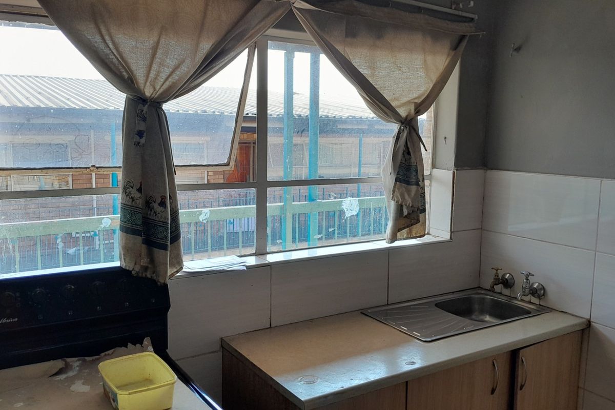 A dated kitchen area featuring a stainless steel sink, tiled splashback, and built-in cabinetry, requiring cosmetic updates to improve functionality and aesthetic appeal.
