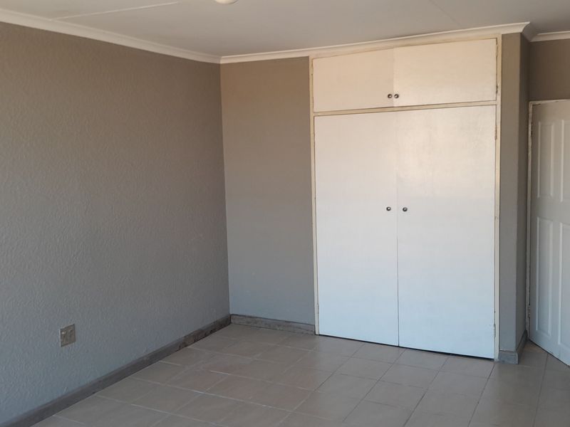 An empty bedroom featuring neutral grey walls, tiled flooring, and white built-in cupboards with overhead storage.