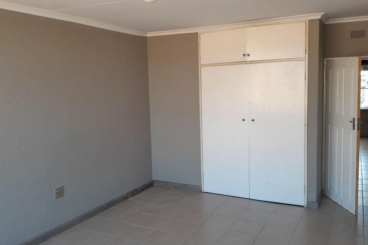 An empty bedroom featuring neutral grey walls, tiled flooring, and white built-in cupboards with overhead storage.