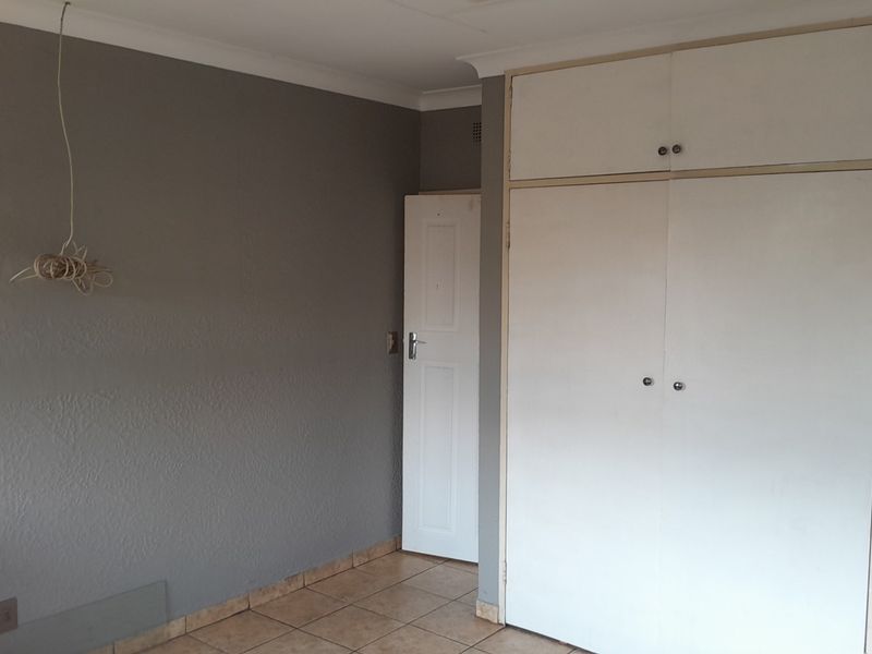 An empty bedroom featuring tiled flooring, built-in cupboards with overhead storage, and grey painted walls.