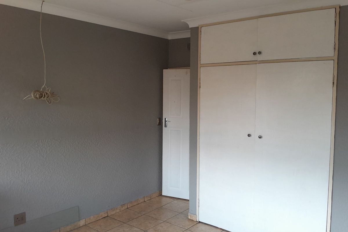 An empty bedroom featuring tiled flooring, built-in cupboards with overhead storage, and grey painted walls.