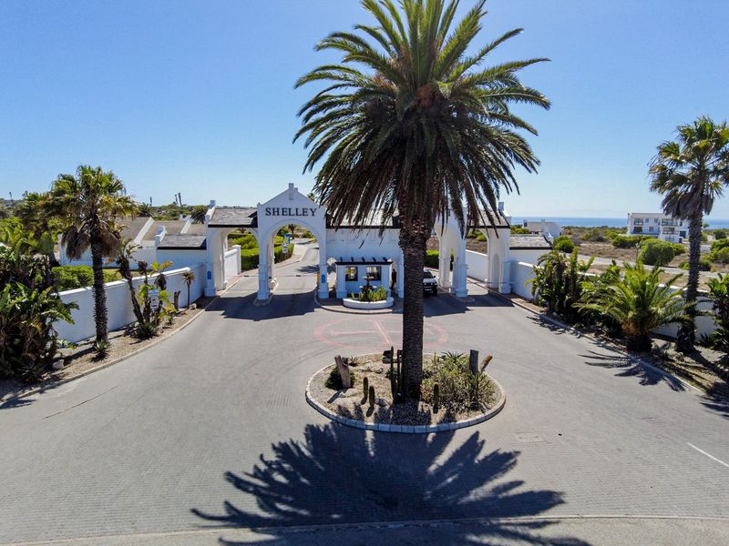 Aerial view of the main gated entrance to the Shelley estate, featuring a paved driveway, security guardhouse, and landscaped roundabout.