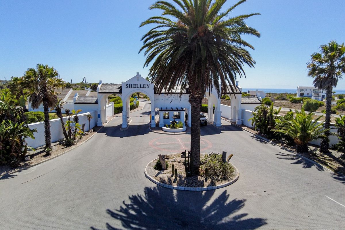 Aerial view of the main gated entrance to the Shelley estate, featuring a paved driveway, security guardhouse, and landscaped roundabout.