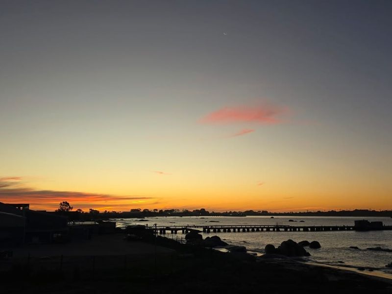 A scenic sunset view over the coastline, featuring calm waters and a distant pier silhouette.