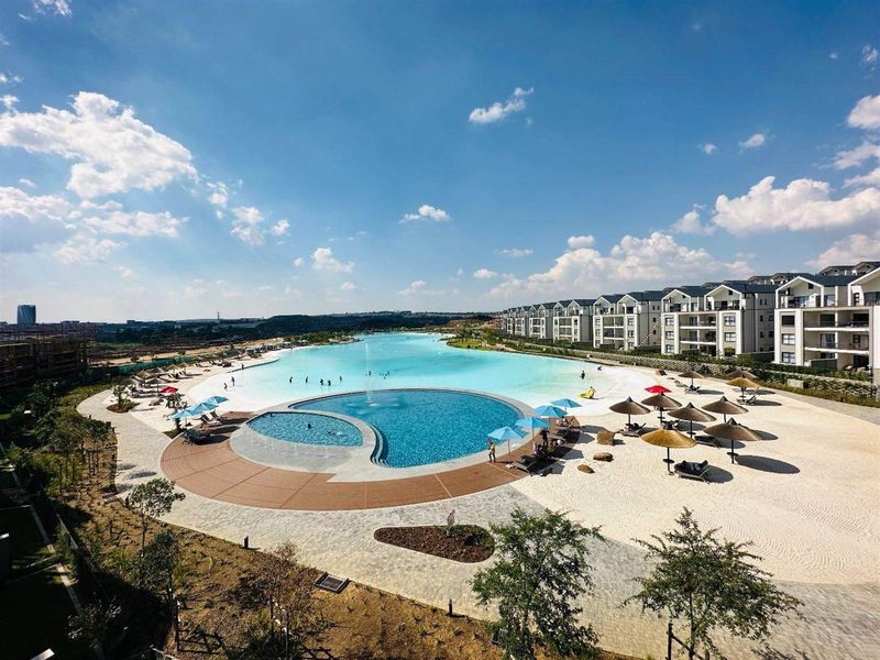 Aerial view of a large communal swimming pool and beach-style leisure area surrounded by modern apartment blocks.