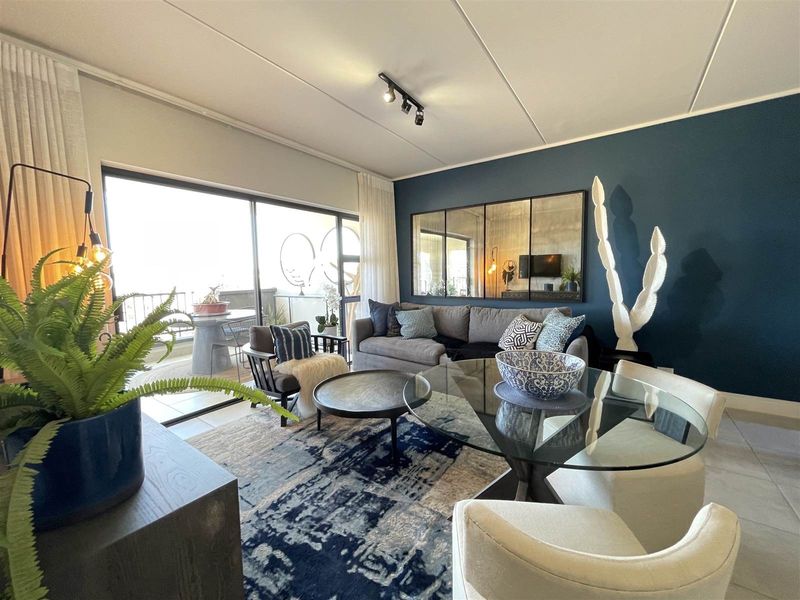 A well-presented open-plan living and dining area featuring tiled floors, modern track lighting, and large sliding glass doors leading to a balcony.
