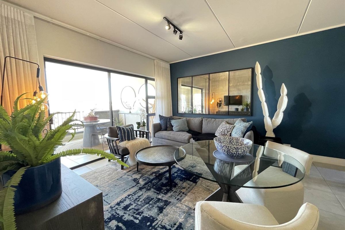 A well-presented open-plan living and dining area featuring tiled floors, modern track lighting, and large sliding glass doors leading to a balcony.
