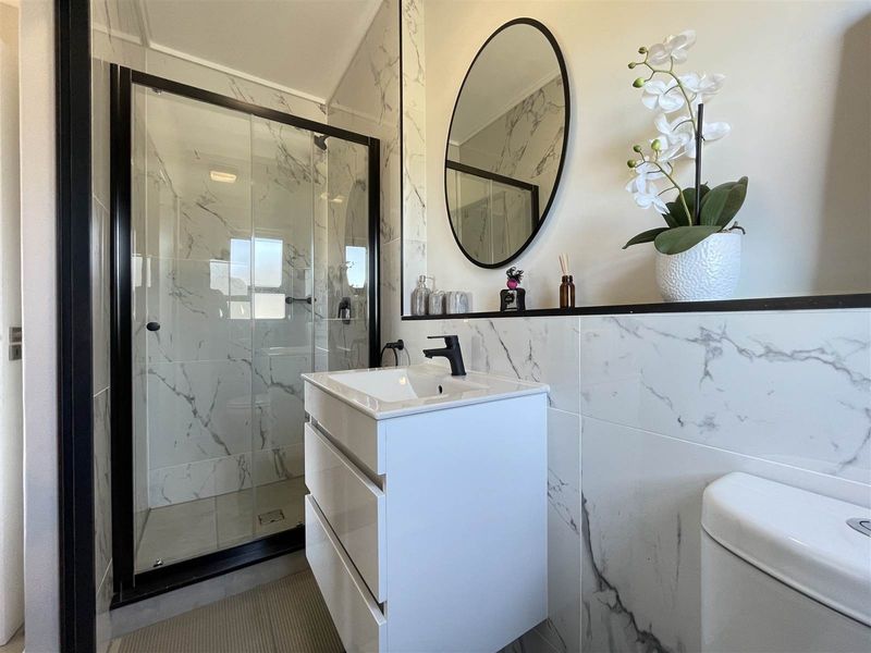 Modern bathroom featuring a walk-in shower with black-framed glass enclosure, marble-look wall tiles, and a contemporary vanity unit with a black mixer tap.