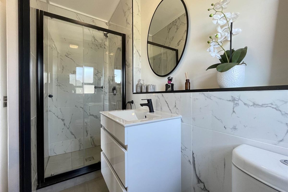 Modern bathroom featuring a walk-in shower with black-framed glass enclosure, marble-look wall tiles, and a contemporary vanity unit with a black mixer tap.
