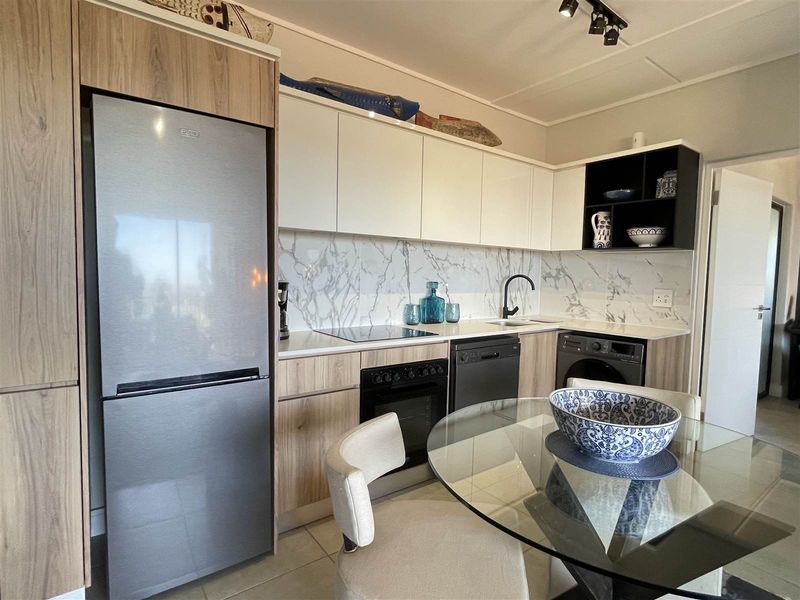 Modern kitchen featuring wood-grain and white cabinetry, marble-look splashback, integrated oven, and hob, offering a clean and functional cooking space.