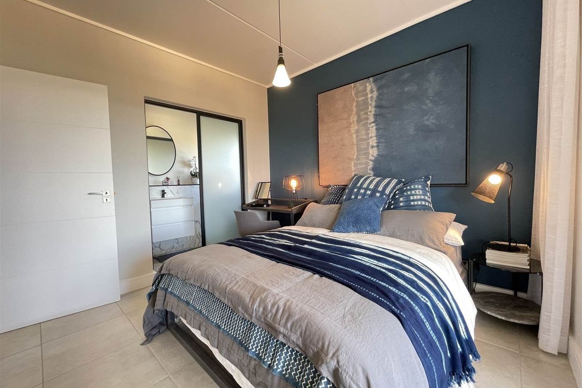 A well-maintained bedroom featuring tiled flooring, a feature wall, and direct access to an en-suite bathroom.