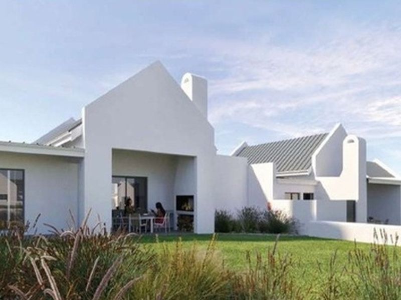 Rear view of a modern white house featuring a covered patio with a built-in fireplace, metal roofing, and a well-maintained garden.