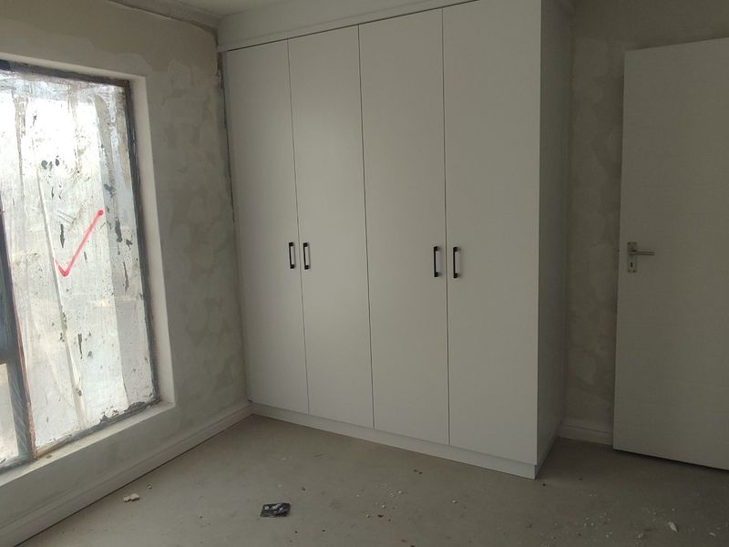 An unfinished bedroom featuring built-in cupboards, requiring final wall finishes and flooring completion to be move-in ready.